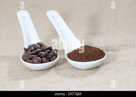 zwei weiße Keramik Löffel mit Bohnen und gemahlenen Kaffee auf Sackleinen Stockfoto