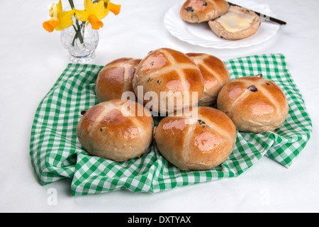 Hot Cross Buns auf eine grüne aufgegebenen Stoff-Serviette mit geschnittenen Brötchen auf einem Teller und Blumen im Hintergrund (6 aus einer Reihe von 24) Stockfoto