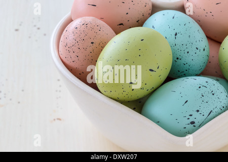 Gesprenkelte Ostereier in einer Vielzahl von Farben. In eine herzförmige Schüssel angeordnet. Stockfoto