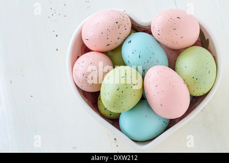 Gesprenkelte Ostereier in einer Vielzahl von Farben. In eine herzförmige Schüssel angeordnet. Stockfoto