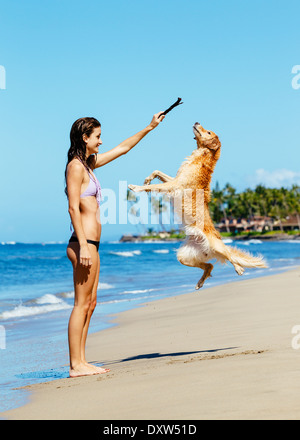 Junge Frau spielt mit ihren entzückenden Golden Retriever am Strand, glücklichen Hund sprang in die Luft. Stockfoto