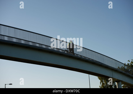 Radfahrer schiebt sein Fahrrad über eine Fußgängerbrücke über der A814 Pointhouse Straße in Glasgow. Stockfoto