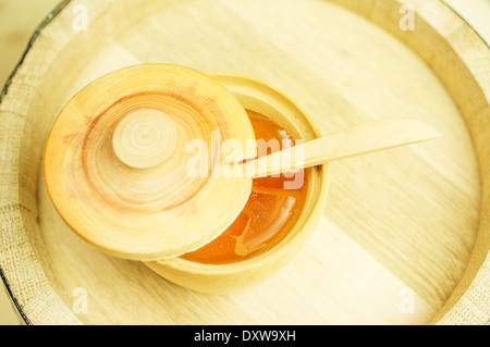 Honig in einer Holzschale mit einem Holzlöffel und Deckel. Hintergrund-Holzfass Stockfoto