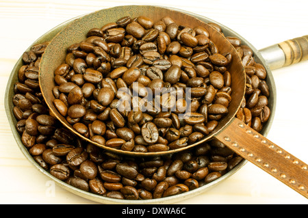 Kaffeebohnen werden in einer kleinen Pfanne in einer großen Pfanne geröstet. Hölzerne Hintergrund. Stockfoto