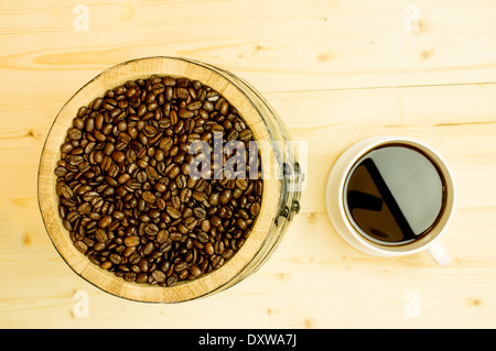 Kaffeebohnen in einem Holzfass. In der Nähe eine große weiße Tasse Kaffee. Stockfoto