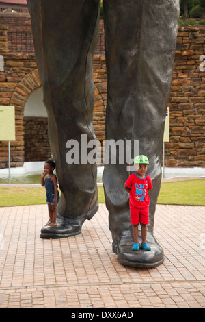 Kinder an den Füßen die riesige Statue von Nelson Mandela vor den Union Buildings Regierungsgebäuden, Pretoria, Gauteng Stockfoto