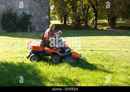 Mann fährt einen roten Rasenmäher (Traktor) im Stadtpark Stockfoto