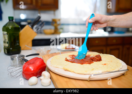 Mann Bürsten Tomatensoße über den Teig auf eine heiße Steinbackplatte für die Herstellung einer hausgemachten pizza Stockfoto