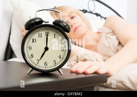 Eine Frau mittleren Alters erreicht für Wecker im Vordergrund der 07:00 lautet. Stockfoto