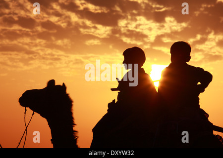 Silhouette Jungs sitzen auf Kamel in Twilight Zeit mit dramatischer Himmelshintergrund Stockfoto