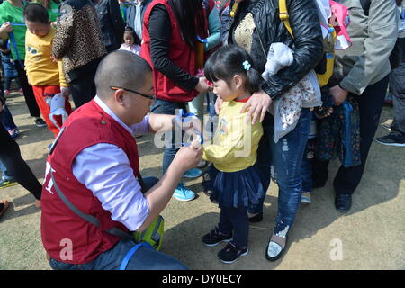 Nanjing, China Jiangsu Provinz. 2. April 2014. Ein freiwilliger bindet eine blaue Schleife, ein Symbol der Sorge um das Handgelenk eines Mädchens mit Autismus bei einem Kind wohl Event in Nanjing, der Hauptstadt der ostchinesischen Provinz Jiangsu, 2. April 2014. Die Veranstaltung am Mittwoch wurde eine lokale Kinder Training Centers organisiert, anlässlich der siebten World Autism Awareness Day. Der Veranstalter hat eine Reihe von interaktiven Aktivitäten in der Hoffnung, Erhöhung der sozialen Fürsorge für Kinder mit Autismus. © Shen Peng/Xinhua/Alamy Live-Nachrichten Stockfoto