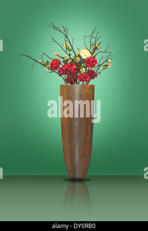 Rote und gelbe Blumen in einer großen Metall Vase auf einem grünen Hintergrund Stockfoto