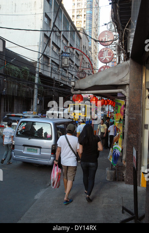 Eine belebte Straßenszene in Chinatown, Manila, mit Passanten, die an farbenfrohen Ladenschildern und hängenden roten Laternen vorbeigehen. Stockfoto
