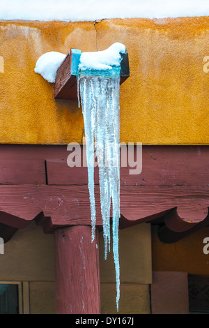 Eiszapfen hängen an einem Canale aus dem Flachdach ein Pueblo Stil Adobe Gebäude an einem Wintertag in Santa Fe, NM Stockfoto