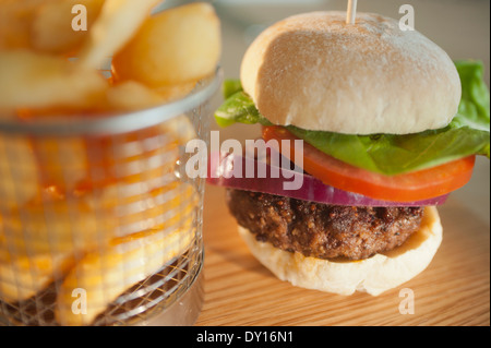 Classic Burger mit Zwiebel-Tomaten-Salat in ein weißes Brot Brötchen mit einer Beilage von Chips oder französische gebratene Kartoffeln. Stockfoto