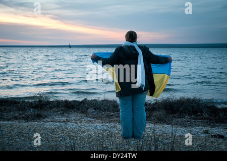 Pro-ukrainische Frau mit einer Nationalflagge steht am Ufer des Donuslaw See, Marines aus U311 Cherkasy Minesweeper zu unterstützen Stockfoto