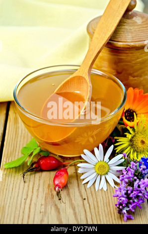 Honig in eine Glasschüssel und einem hölzernen Topf, Löffel, Hagebutte Beeren, Blumen, Serviette auf dem Hintergrund der Holzbretter Stockfoto