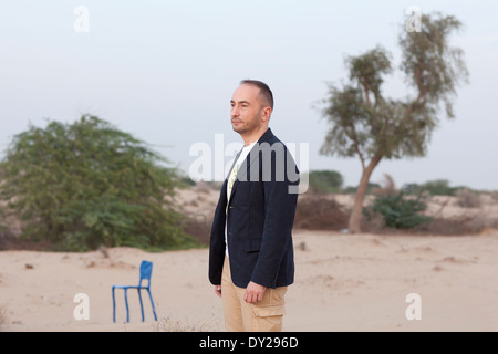 Cyril Zammit, Direktor der Messe Design Days Dubai steht für ein Porträt in der Wüste mit seinem Stuhl, entworfen von Maarten Baas. Stockfoto