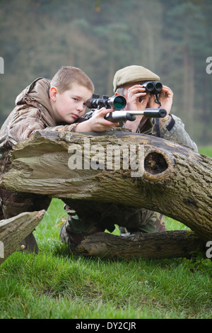 Ein kleiner Junge mit einem Gewehr schießen Schädlinge auf dem Lande mit seinem Jagdaufseher Vater neben ihm. Stockfoto