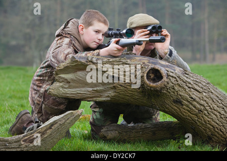Ein kleiner Junge mit einem Gewehr schießen Schädlinge auf dem Lande mit seinem Jagdaufseher Vater neben ihm. Stockfoto