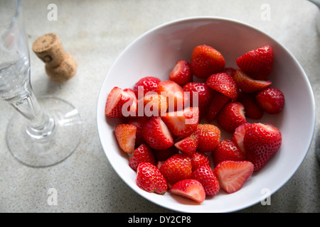 Weiße Schale mit geschnittenen Erdbeeren auf weiße Tischwäsche mit Sektkorken und Glas bei einer Hochzeitsfeier Stockfoto