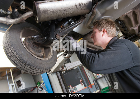 Ein Techniker prüft die technischen Zustand unter einer angehobenen Auto auf einer Brücke in einer garage Stockfoto