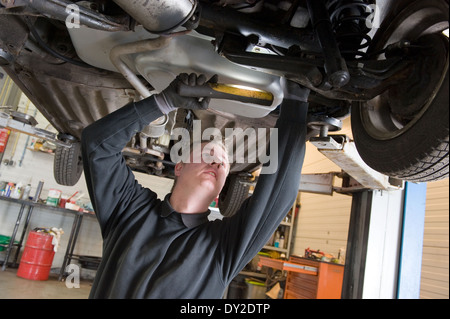 Ein Techniker prüft die technischen Zustand unter einer angehobenen Auto auf einer Brücke in einer garage Stockfoto