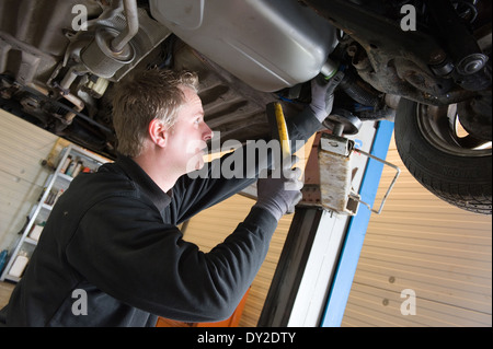 Ein Techniker prüft die technischen Zustand unter einer angehobenen Auto auf einer Brücke in einer garage Stockfoto