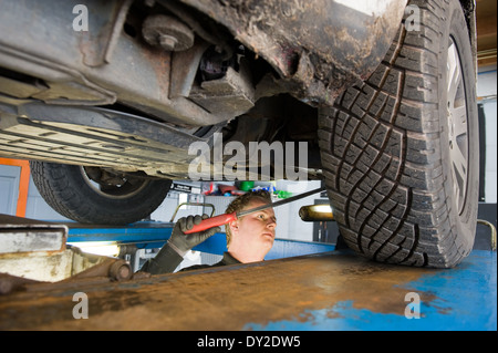 Ein Techniker prüft die technischen Zustand unter einer angehobenen Auto auf einer Brücke in einer garage Stockfoto