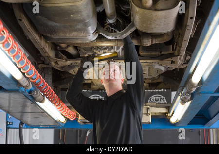 Ein Techniker prüft die technischen Zustand unter einer angehobenen Auto auf einer Brücke in einer garage Stockfoto