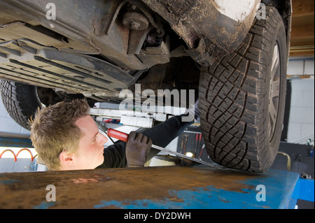 Ein Techniker prüft die technischen Zustand unter einer angehobenen Auto auf einer Brücke in einer garage Stockfoto