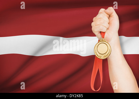 Sportler halten Goldmedaille mit Flagge auf Hintergrund - Republik Lettland Stockfoto