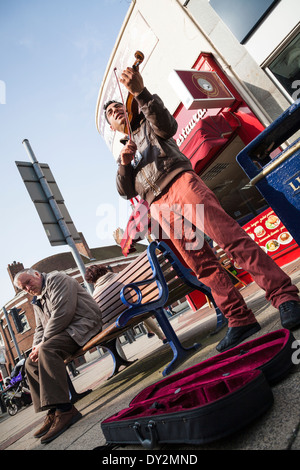 Straße Straßenmusiker spielt Geige neben Mann auf Bank. Stockfoto