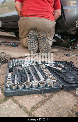 Eine schmutzige Mechaniker arbeitet an einem Fahrzeug mit seinen Werkzeugen im Vordergrund Stockfoto