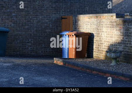 Wheelie-Behälter, braunen und blauen Mülltonnen sitzen nebeneinander hinter dem Haus Stockfoto