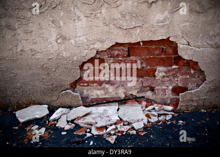 Ziegel hinter einer Betonmauer ist erschüttert und offenbart. Stockfoto