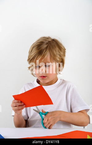 junge schneidet rote farbiges Papier mit einer Schere Stockfoto