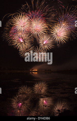 Ausbrüche von Orange und rosa Feuerwerk spiegelt sich in einem trüben See Stockfoto