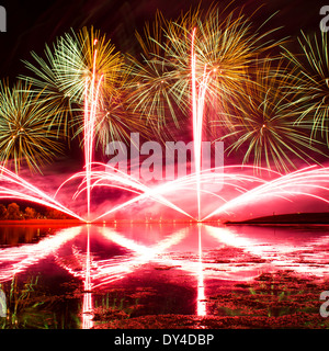 Ausbrüche von Grün, Orange und rosa Feuerwerk spiegelt sich in einem trüben See Stockfoto