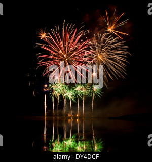 Ausbrüche von rot, Orange und grün Feuerwerk spiegelt sich in einem trüben See Stockfoto