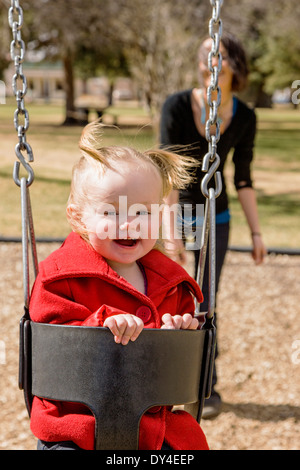 Schöne junge Mutter auf Park Spielplatz Schaukeln mit liebenswert, niedlich 16 Monate Babymädchen spielen Stockfoto