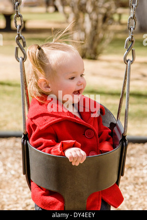 Liebenswert, niedlich 16 Monat Mädchen schwingen auf einem Park-Spielplatz Stockfoto