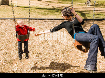 Schöne junge Mutter auf Park Spielplatz Schaukeln mit liebenswert, niedlich 16 Monate Babymädchen spielen Stockfoto