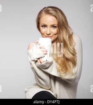 Nettes Lächeln auf den Lippen Mädchen in übergroßen Pullover. Schönen lächelnden jungen Frau hält eine Tasse warmen Tee oder Kaffee. Stockfoto