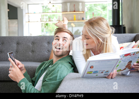 Mann mit Smartphone und Frau liest Buch auf Sofa