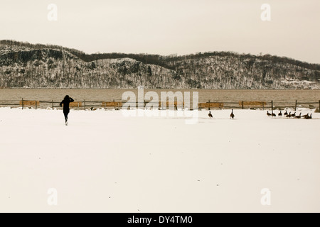 Frau läuft über schneebedeckten Feld in Richtung Fluss Stockfoto