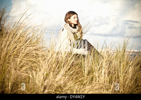 Junge Frau sitzt in Sanddünen, Bournemouth, Dorset, Großbritannien Stockfoto