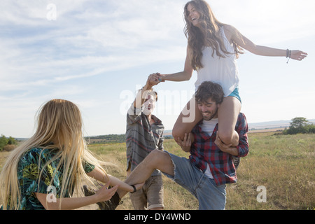 Vier Freunde spielen, Mann, die Frau auf den Schultern tragen Stockfoto