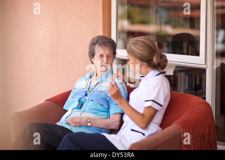 Pflege Assistentin im Gespräch mit älteren Frau auf sofa Stockfoto