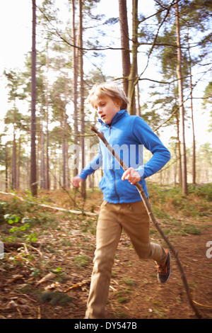 Junge läuft mit einem Stock im Wald Stockfoto